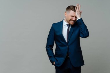 Takım elbiseli umutsuz iş adamı kötü haber alıyor, alnına elinle dokunuyor ve gri arka planda dururken üzülüyor. CEO 'nun işte sorunları var.