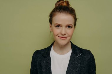 Stüdyoda poz veren, güler yüzlü, modaya uygun giyinmiş genç bayan öğrencinin yanına yaklaşın. Sevimli, mutlu genç kız kameraya hafifçe gülümseyen, sakin ve tatmin olmuş bir şekilde bakıyor.