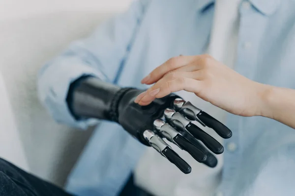 Hands of handicapped girl setting up her bionic arm and pressing buttons. Young european woman with cyber hand at home. Modern robotic bionic prosthesis. Futuristic technology and engineering concept.