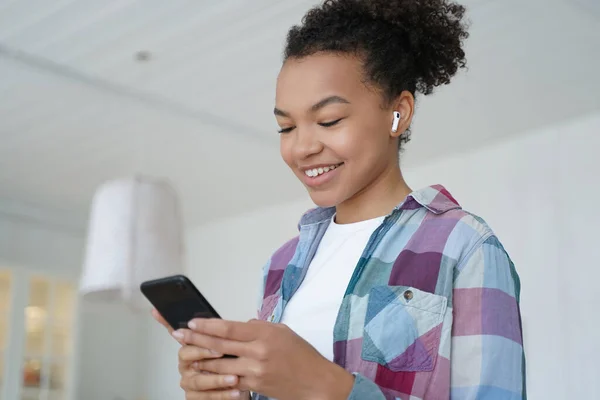 stock image Music listening in airpods on mobile phone. Joyful teenage african american girl enjoying favourite song in wireless earphones. Student is browsing internet and social media on smartphone.