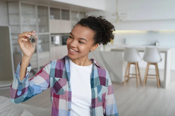stock image Happy teenager is homeowner in living room of new residence. Cute young african american girl is holding key from new apartment. Mortgage loan and real estate purchase conceptual image.