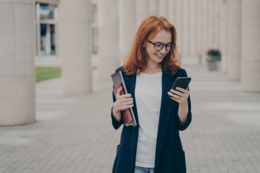 Genç, kırmızı saçlı, şık giyinmiş, cep telefonu kullanan, mesajlaşan ya da e-postalarını kontrol eden, sıkı çalışan, dizüstü bilgisayarlı, not defteri tutan bir iş kadını.
