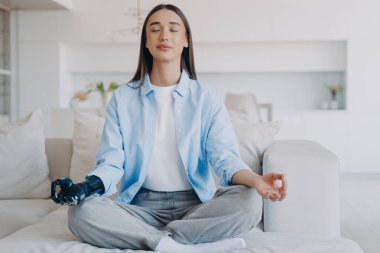 Serene engelli kadın nilüfer çiçekli koltukta oturuyor. Bayan, sabah yogasını gözleri kapalı yapıyor. Çekici Avrupalı kızda miyoelektrik siber protez var. Modern yapay kol.