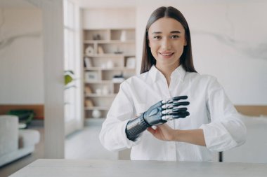Handsome european girl has high tech carbon electronic hand. Disabled young woman is assembling bionic arm with hand. Girl is setting the prosthesis functions. Modern technology for wellbeing.