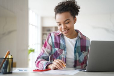 Happy young biracial girl student learning at laptop look at smartphone screen chatting in social network. Schoolgirl teenage distracted from school tasks, homework. Gadget addiction concept.
