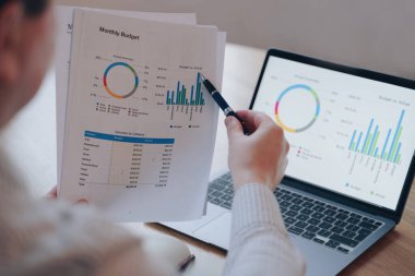 Bilgisayarda ve kağıtta finansal yuvarlak diyagram. Adam evrak işleriyle uğraşıyor, internetten satmakla meşgul. Çevrimiçi ticaret. Bilgisayarın ve telefonun masadaki görüntüsü. Aylık bütçe planlaması.