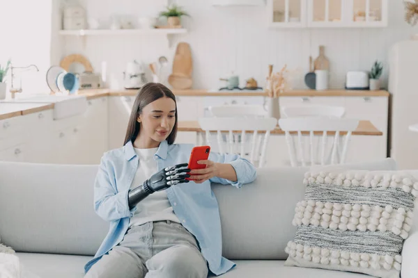 stock image Attractive handicapped woman is texting on smartphone. Disabled european woman browsing internet. Happy girl is holding the phone with bionic artificial arm. Equality and life quality concept.