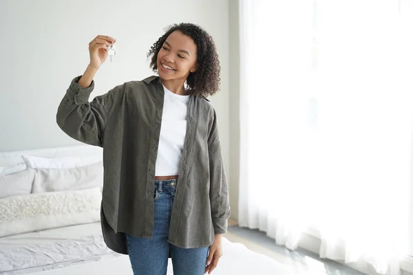 Curly african american girl is holding key from new home. Teenager gets new apartment key. Young woman is standing in modern room. Mortgage loan and real estate purchase conceptual image.