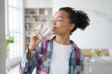 African american woman enjoy drinking pure crystal filtered potable water. Thirsty female with eyes closed swallow mineral aqua from glass at home kitchen. Thirst, healthy lifestyle, body care concept