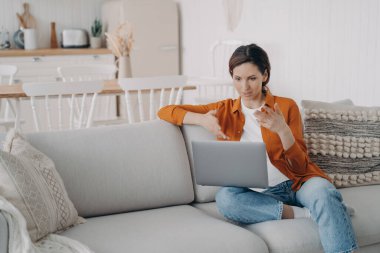 Genç İspanyol kadının evde online konferansı var. Bilgisayarlı kız internet toplantısında konuşuyor. Güzel bayan kanepede oturmuş tartışıyor. Karantina sırasında çalışıyor.