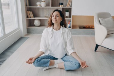 Kız lotus pozunda gözleri kapalı oturuyor. Mutlu Avrupalı kadın evde yoga ve meditasyon yapıyor. Sabah jimnastiği ve zen. Stres atma, refah ve barış kavramı.