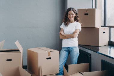 Satisfied woman unpacking boxes. Attractive girl in new apartment. Young woman in jeans and white t-shirt. Relocation, delivery service and new apartment concept.