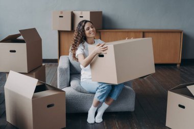 Gururlu Avrupalı kız yeni evine taşındı. Mutlu genç kadın yalnız hareket ediyor. Hanımefendi koltukta, paketlenmiş karton kutuların arasında oturuyor. Bağımsızlık, yaşam seçimi ve başarı kavramı.