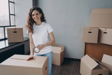 Mover koli bandıyla kargo paketliyor. Genç bayan koli bandıyla karton kutuları paketliyor. Mutlu İspanyol kız yerini değiştiriyor. Servis çalışanı nakliye için kutu hazırlıyor.
