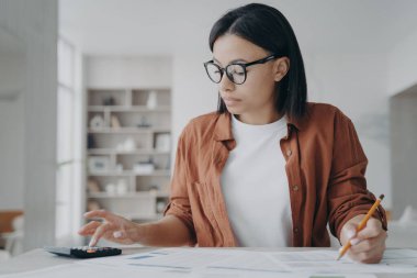 Gözlüklü kadın ev bütçesini yönetir. Tasarruf giderlerini hesaplar. Finansal evraklarla ciddi kadın işleri, kira hesabı, ipotek ücretleri, evde masa başında oturmak..