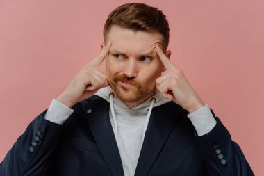 Odaklan ve konsantre ol. Gündelik giyinmiş genç bir adam karar vermeye çalışıyor, düşünceli bir ifadeyle yan yan bakıyor, parmaklarını şakaklara dayayıp doğru çözümü bulmaya çalışıyor.