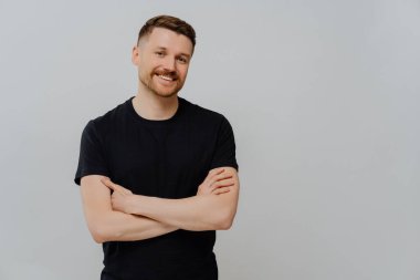 Kendinden emin bir adamın yatay çekimi kollarını kavuşturur. Gülümser, rahatça giyinir. Boş arkaplan ve boş arkaplan pozlarından zevk alır. Stüdyodaki yakışıklı erkek model.