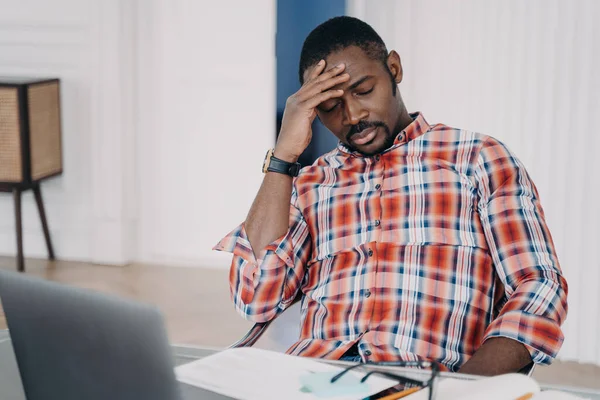 Tired african american businessman suffer from headache at workplace at laptop. Frustrated overworked black male guy touching head thinking about business problem, closed eyes. Stress at work concept