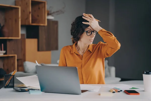 Frustrated Italian female employee stressed about mistake or problem with computer, got bad news from office. Tired nervous spanish woman working remotely online from home. Pressure at work concept