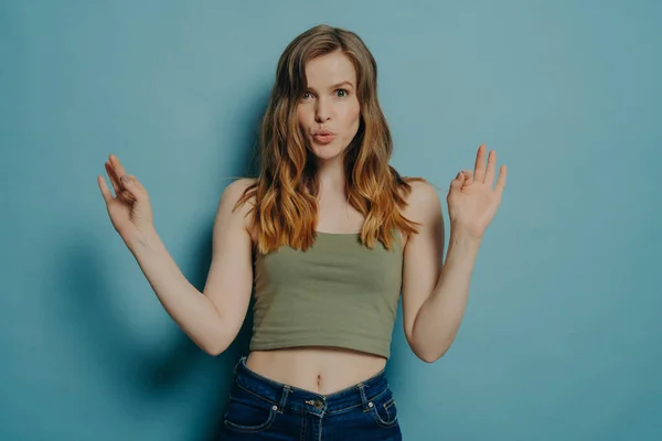 Young confident european woman showing okay gesture with both hands and pouting lips isolated over pastel blue studio wall background, female saying that everything is fine. Body language concept