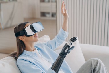 Sanal gerçeklik gözlüklü biyonik kollu mutlu Avrupalı kız evde tedavi görüyor. Özürlüler için psikolojik rehabilitasyon. Sağlık hizmetleri yenilikleri iyileştirme teknolojisi.