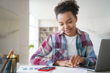 Yakışıklı afro kız evde uzaktan eğitim görüyor ve ödev yapıyor. Genç bir kız bilgisayarın önünde oturmuş online sınav yaptırıyor. Yakınlaştırma yoluyla okulda veya üniversitede uzaktan eğitim.