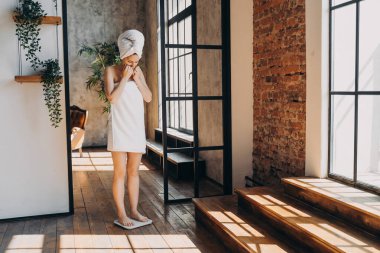 Weight gaining concept. Frustrated slim european woman taking step onto scale to measure her weight. Girl wrapped in towel after bathing has time at spa. Stressed woman checking weight after shower.