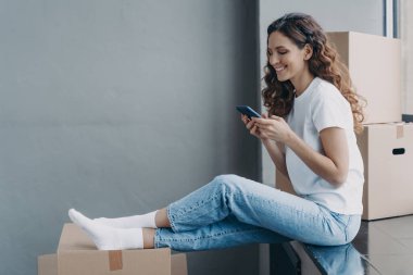 Mutlu, çekici İspanyol kadın karton kutularla eşikte oturuyor. Kız cep telefonundan mesaj atıyor. Genç bayan kutuları boşaltıyor. Mesafe arkadaşlığı ve yer değiştirme kavramı.