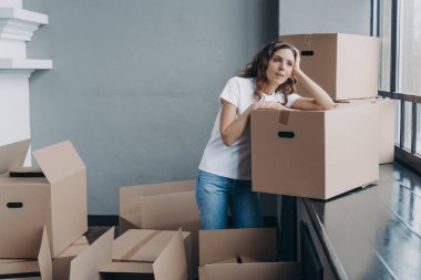 Girl is dreaming while sitting on floor in new apartment. Young woman enjoying view looking at the window. Happy attractive hispanic woman unpacking boxes. Concept of future and perspective.