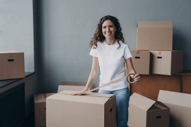 Mutlu genç bayan koli bandıyla kutuları paketliyor. Çekici bayan karton kutuları koli bandıyla paketliyor. Nakliye işçisi nakliye ve depolama için kargo hazırlıyor..