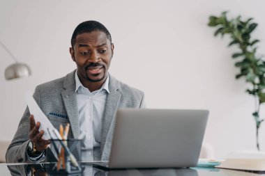 Perplexed african american male worker looking at laptop screen received dismissal notice. Puzzled black guy businessman reading bad news in email or having problem with computer.