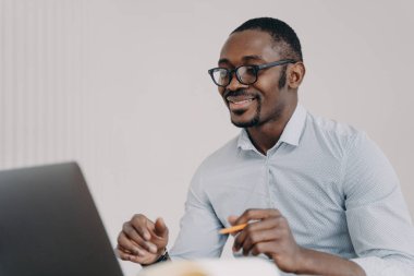 Afrikalı Amerikalı adam kameranın önünde konuşuyor. Resmi kıyafetli mutlu genç iş adamı müşterisiyle ya da iş arkadaşlarıyla görüntülü konuşma yapıyor. Uzak çalışma ya da ev kavramında uzak ders.