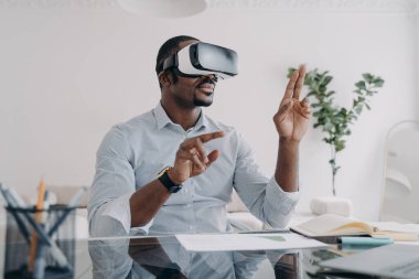 VR kulaklıklı bir iş adamı sanal düğmelere basar. Freelancer tasarım projesi üzerinde çalışıyor. Evinde fütürist vr kulaklık takmış Afrikalı Amerikalı bir adam. İş ve yaratıcılık için modern dijital teknoloji.