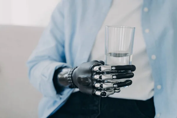 Morning routines of disabled person. Girl is using futuristic robotic arm prosthesis and holding glass of water at home. Modern bionic prosthesis. Healthy lifestyle after amputation surgery.