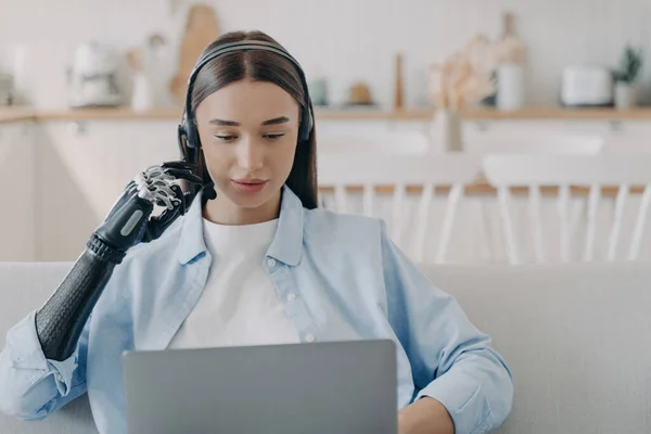 Disabled young woman in headset has online meeting with computer. European handicapped girl has equal rights. Remote manager at home on quarantine. Modern bionic prosthesis technology.