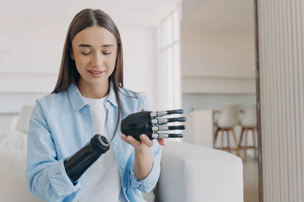 Disabled young woman is assembling bionic arm with hand. Prosthesis is connecting in wrist joint. Cyber sensor hand has processor chip and buttons. European girl has high tech carbon electronic hand.