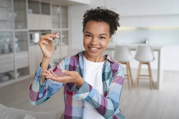 New apartment buyer. Happy teenager is homeowner in living room of new residence. Carefree african american girl is holding house key and smiling. Mortgage loan and relocation conceptual image.