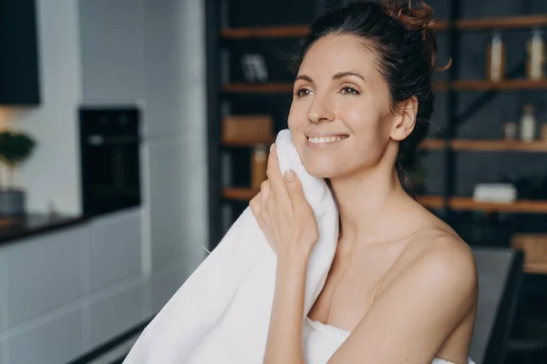 stock image Attractive hispanic woman is wiping face with towel after washing. Happy girl takes shower at home and doing skin care. Hygiene, freshness and female spa procedures. Beauty routine.