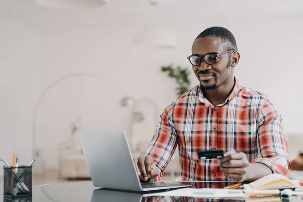 Szczęśliwy Afroamerykanin Okularach Kupuje Online Domu Pomocą Laptopa Karty Kredytowej — Zdjęcie stockowe
