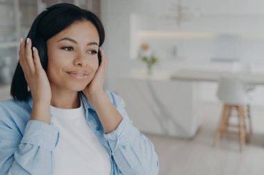 Genç melez romantik bayan kulaklıkla radyo dinliyor, hayal kuruyor ve gülümsüyor. Müzikten zevk alan mutlu Avrupalı kız. Evde hafta sonunun tadını çıkarıyorum. Duygular ve rahatlama.