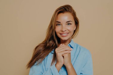 Gülümseyen, uzun kahverengi saçlı, sıradan giyinmiş, el ele tutuşan mutlu bir şekilde kameraya bakan neşeli bir öğrenci. Güzel beyaz bir kadının stüdyo fotoğrafı.