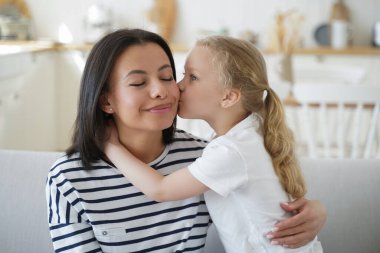 Little kid girl foster daughter kiss cuddle mother showing love at home. Smiling mom enjoy cute tender moment together with her adopted child. Happy motherhood, adoption of children. clipart
