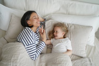 Genç anne küçük kızıyla yatak odasında dinleniyor. Beyaz kadın ve çocuk gülümsüyor ve birlikte uykuya dalıyorlar. Anne ve çocuk uyanıyor. Ebeveynlik ve ilişki kavramı.