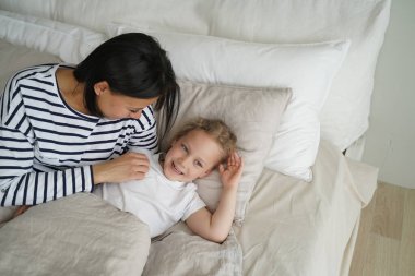 Kafkasyalı genç anne küçük tatlı kızıyla yatak odasında dinleniyor. Kadın ve çocuk mutlu ve birlikte uyuyorlar. Anne ve çocuk evde uyanıyor ve dinleniyorlar. Gündüz uykusu.