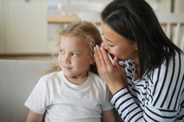 Genç anne küçük kızına bir sır fısıldıyor. Sevgi dolu bir ailenin mutlu anları olur. Genç Avrupalı anne ve çocuk evdeki oturma odasında. Bağlanma ve birliktelik kavramı.