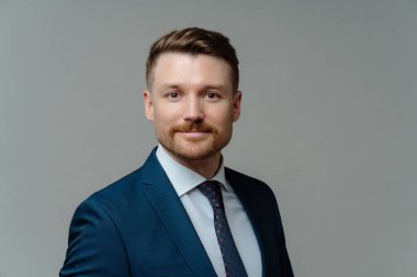 Resmi kıyafet giymiş ciddi sakallı erkek yöneticinin stüdyo fotoğrafı gri arka planda doğrudan kameraya bakıyor. Yakışıklı işveren iş toplantısına hazır. Görev konsepti.