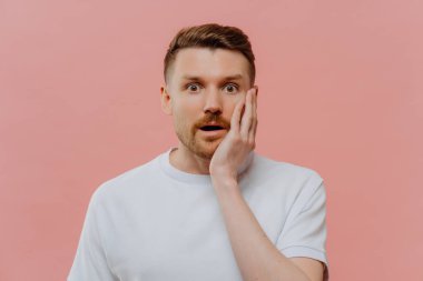 Şaşırmış, tıraşsız kızıl saçlı adamın portresi şaşırmış bir ifadeyle kameraya bakarken Pastel Pembe Stüdyo 'nun arka planında tek başına dururken merak ettiği şaşkınlığı ifade ediyor..