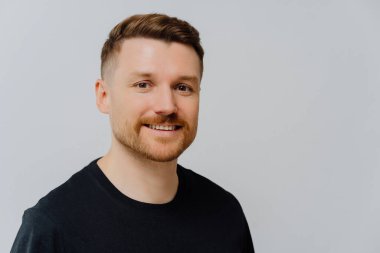 Hayatın tadını çıkarıyorum. Gri duvara karşı siyah tişört giyerken kameraya pozitif yüz ifadesiyle bakan mutlu, keyifli, tıraşsız bir adamın portresini yakından çek. İnsanlar ve olumlu duygular