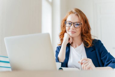 Yatay atış hoş görünümlü başarılı profesyonel kadın avukat istemcileri durumda öğrenir, modern dizüstü bilgisayar, giymiş resmi giyim ve şeffaf gözlük çalışır, ofiste pozlar