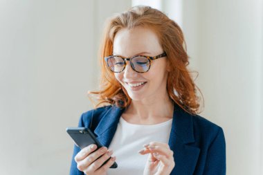 Şık giyim, cep telefonu, ileti almak mutlu akıllı pozitif kadın girişimci kar büyütmekten öğrenirse, Kızıl saçlı, gülümseyerek mutlu bir şekilde sahip, modern ofiste kapalı teşkil etmektedir